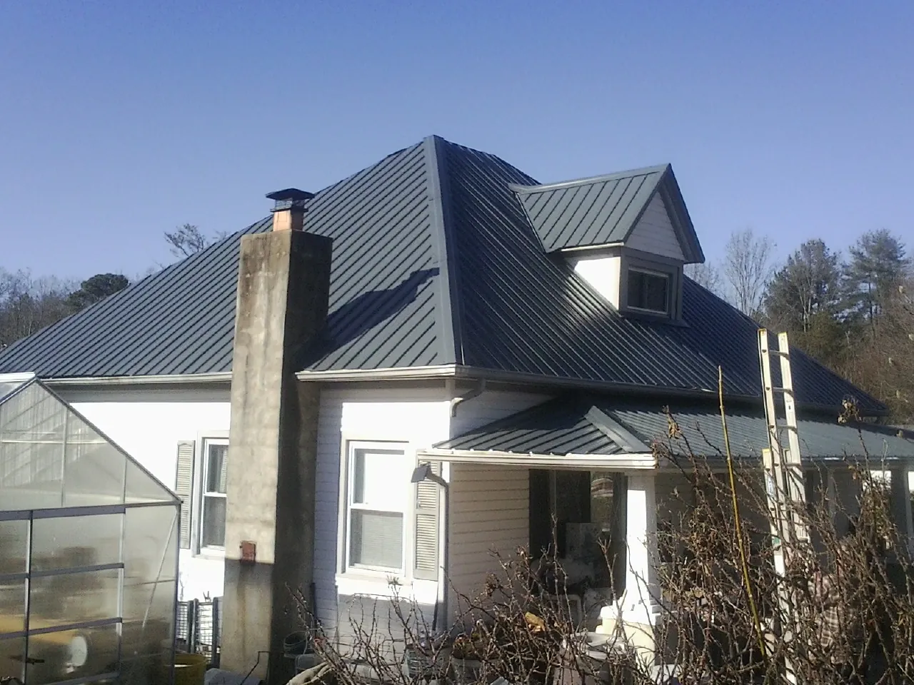Dark blue standing seam metal roof on a white farmhouse with dormer — Slate & Tile Roof Repair by Roofing Brothers in Oakmont