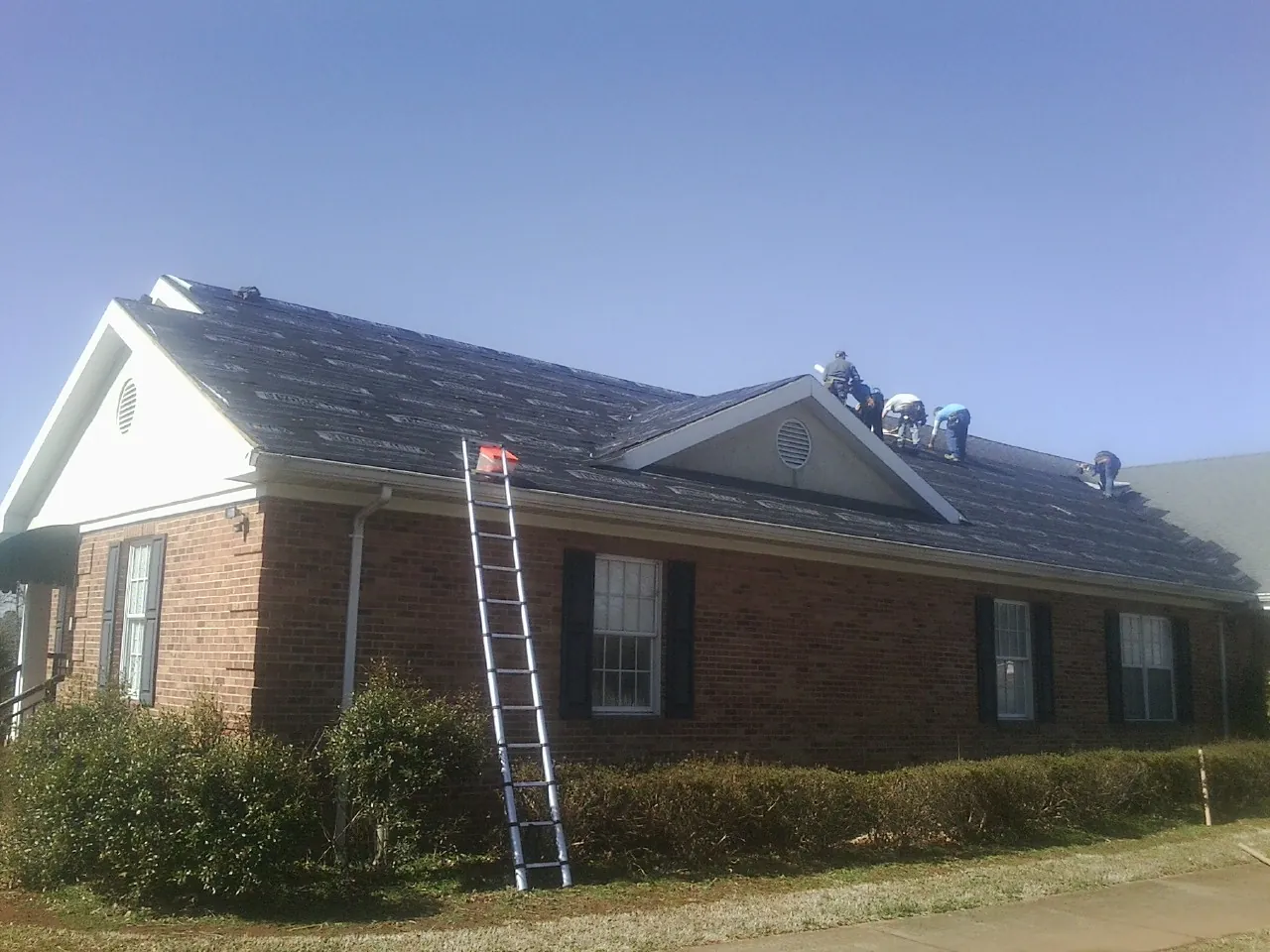 Crew tearing shingles off a brick ranch roof with a ladder set — Metal Roof Repair work by our crew in Oakmont