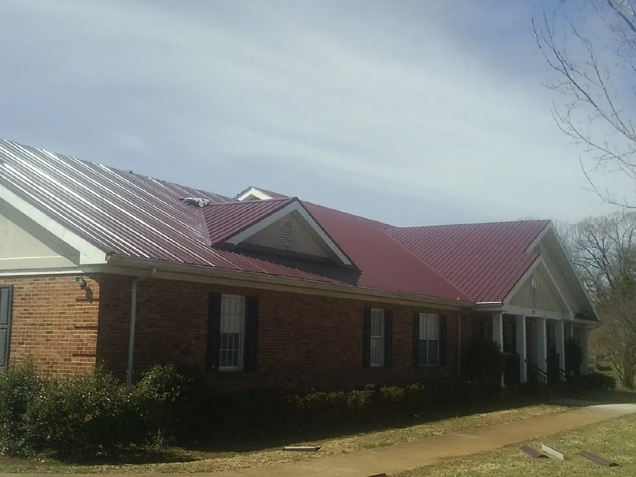 Red metal roof with gabled entries on a long brick building, from a Hail Damage Roof Repair job in Oakmont
