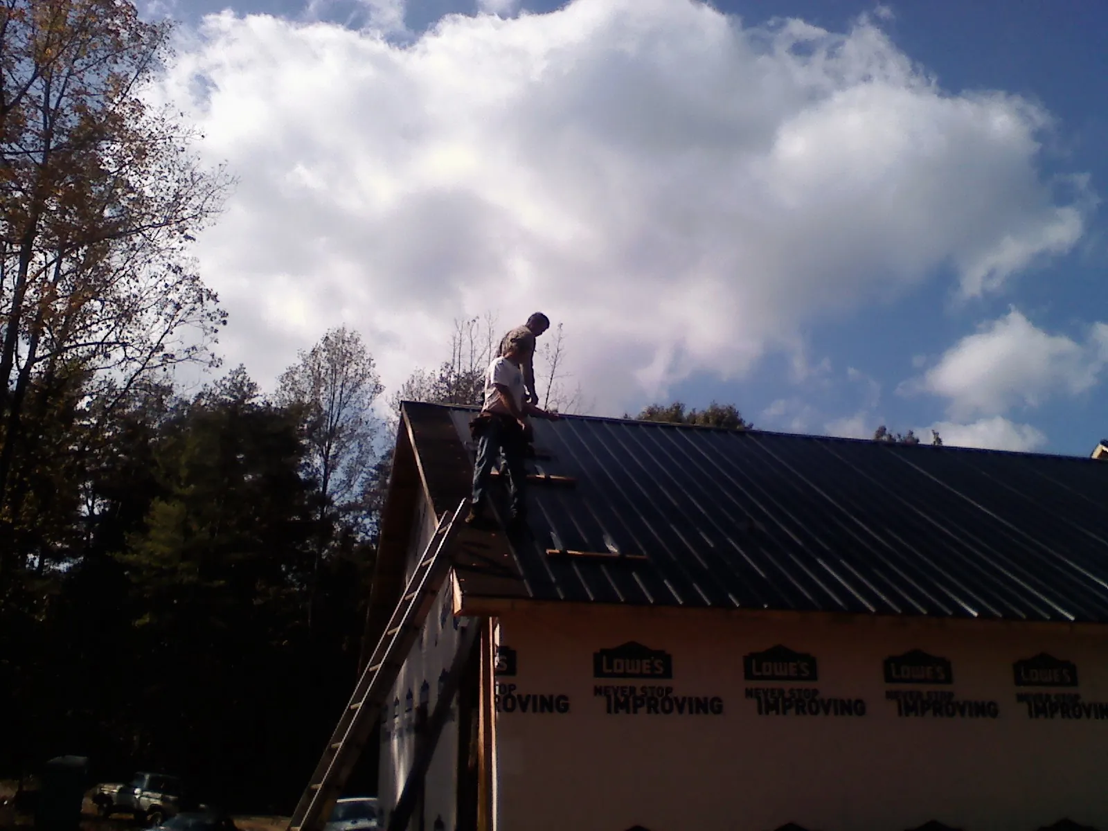 Roofer fastening dark metal panels high against a cloudy sky, from a Roof Inspection job in Oakmont