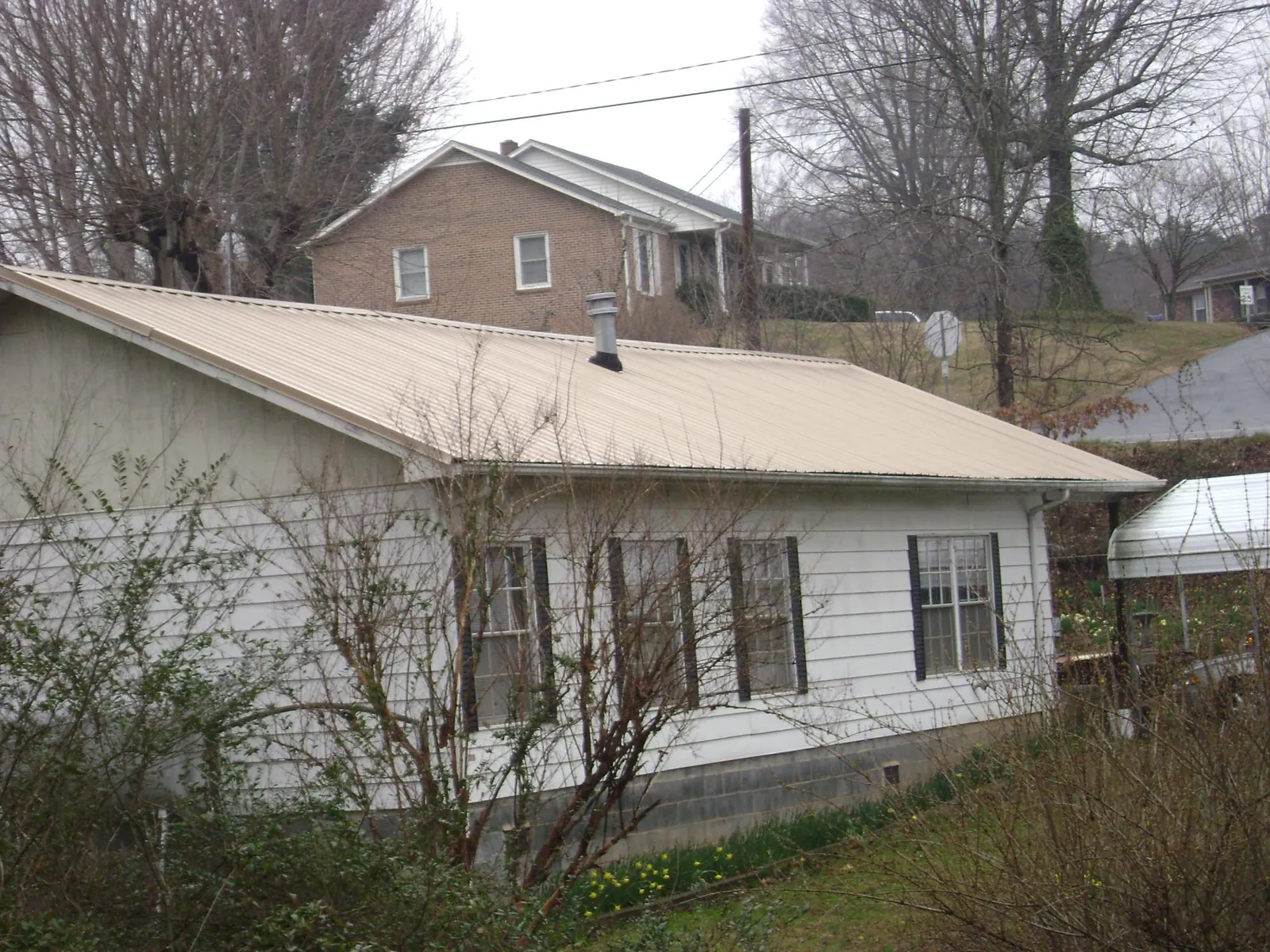 Tan metal roof on a white sided house set into a hillside — Commercial Roofing by Roofing Brothers in Oakmont